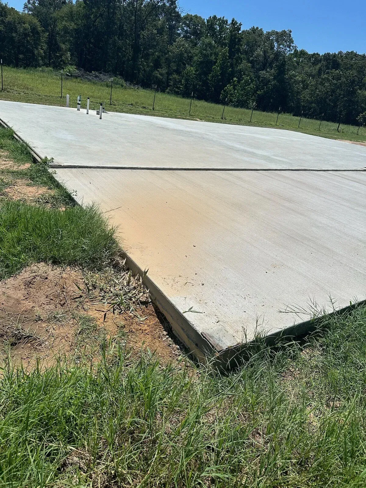 Edge of a freshly poured concrete slab beside a grassy lot